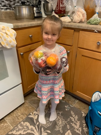 A child from Iryana’s family smiling with a bag of fruit