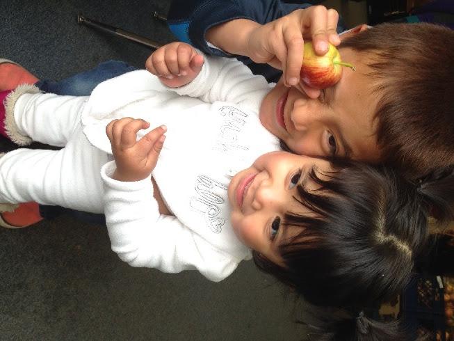 Two children embracing while one holds a small apple in front of his eye