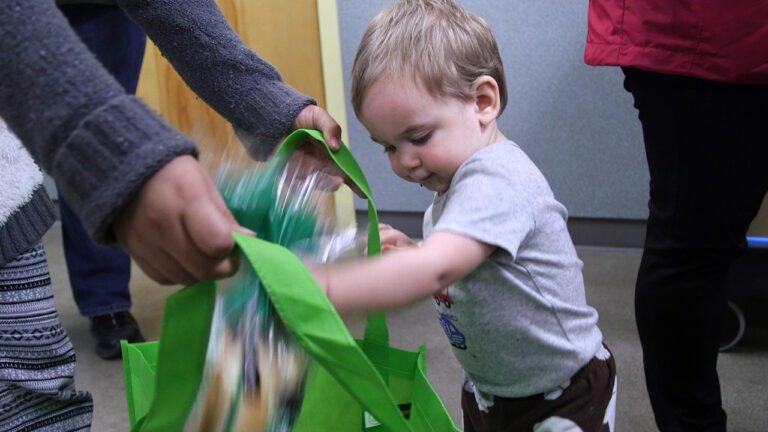 a toddler adds items to a grocery bag at the food pantry