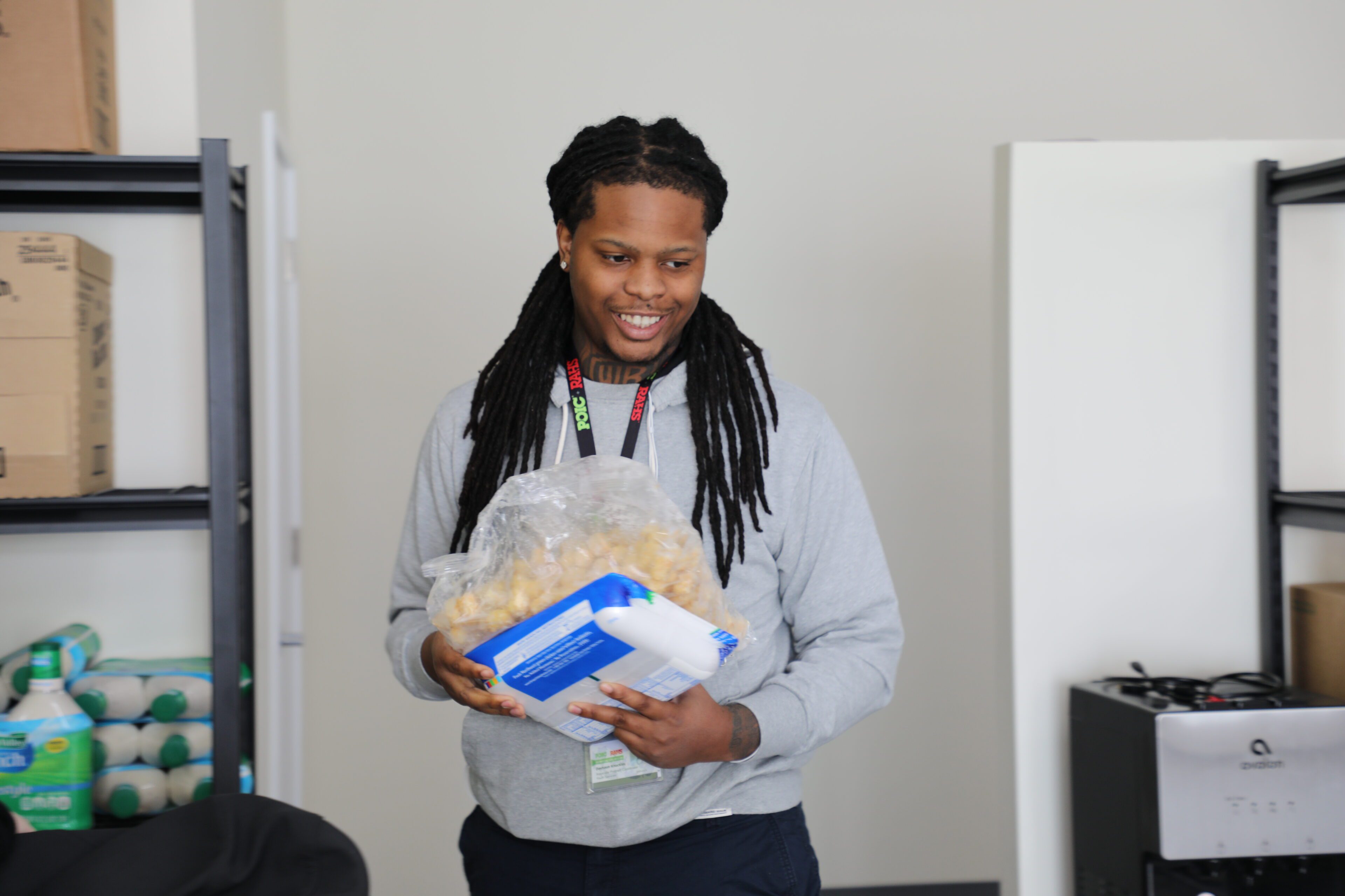 DeShaun Knuckles smile while holding a packet of meat and frozen goods to demonstrate the meal kits that POIC assembles for students.