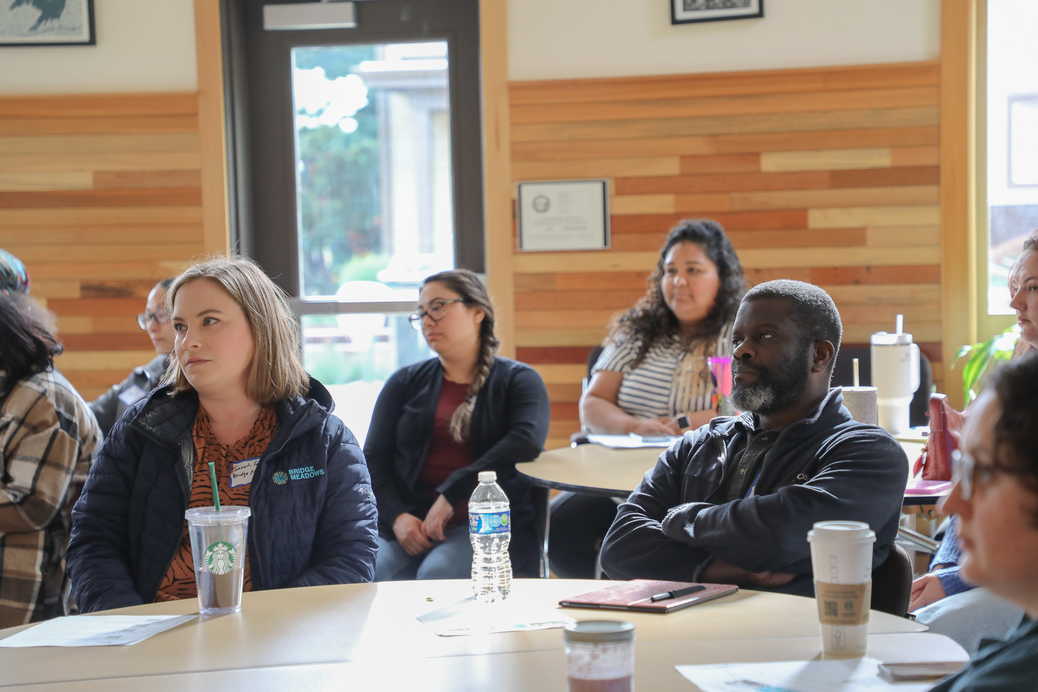 Photo of people seated at round tables listening to the presenters at a training session for staff who work at PCL grantee partner organizations.