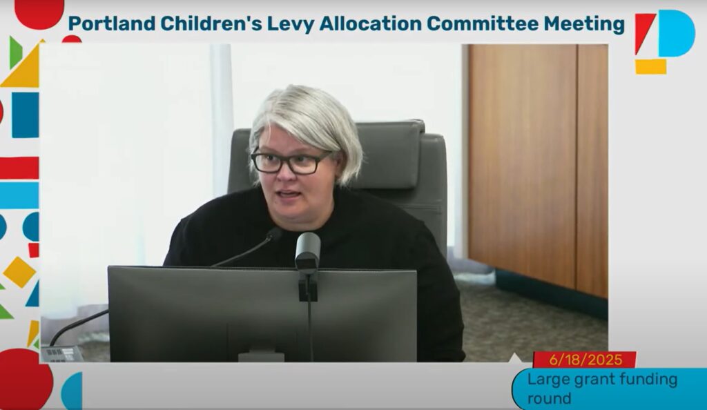 photo from June 18, 2025 Allocation Committee meeting. Multnomah County Commissioner Meghan Moyer, a member of the Allocation Committee, is seated at a dais in front of a computer monitor and microphone speaking. Moyer is wearing a black shift and eyeglasses.