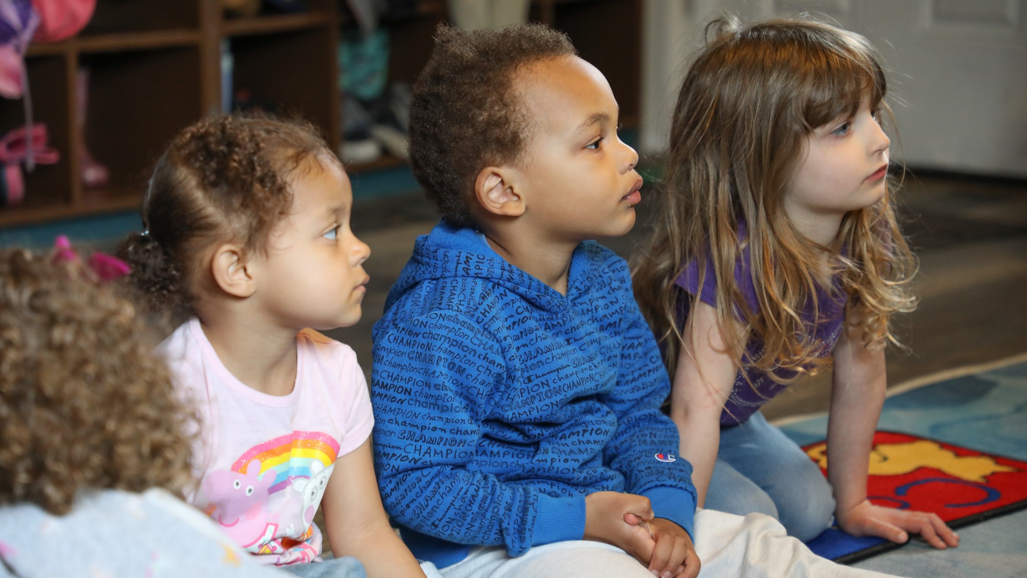 photo of three young children sitting and listening during storytime at Happy Go Lucky Childcare