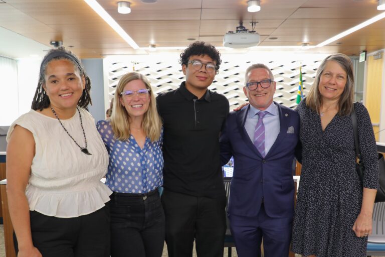 photo of five people standing in a row with arms around each other and smiling at the camera