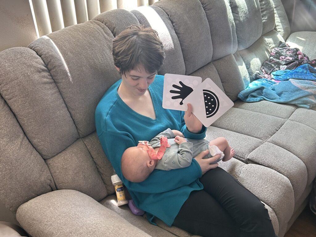 TC, an Echo program participant, holds up pictures of symbols while engaging with their baby. Photo courtesy of Janus Youth Programs